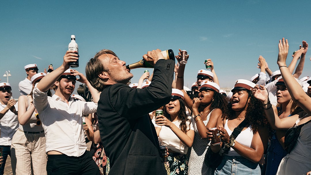 Mads Mikkelsen as Martin, drinking from a bottle surrounded by partying students in the final scene of Thomas Vinterberg’s film Another Round