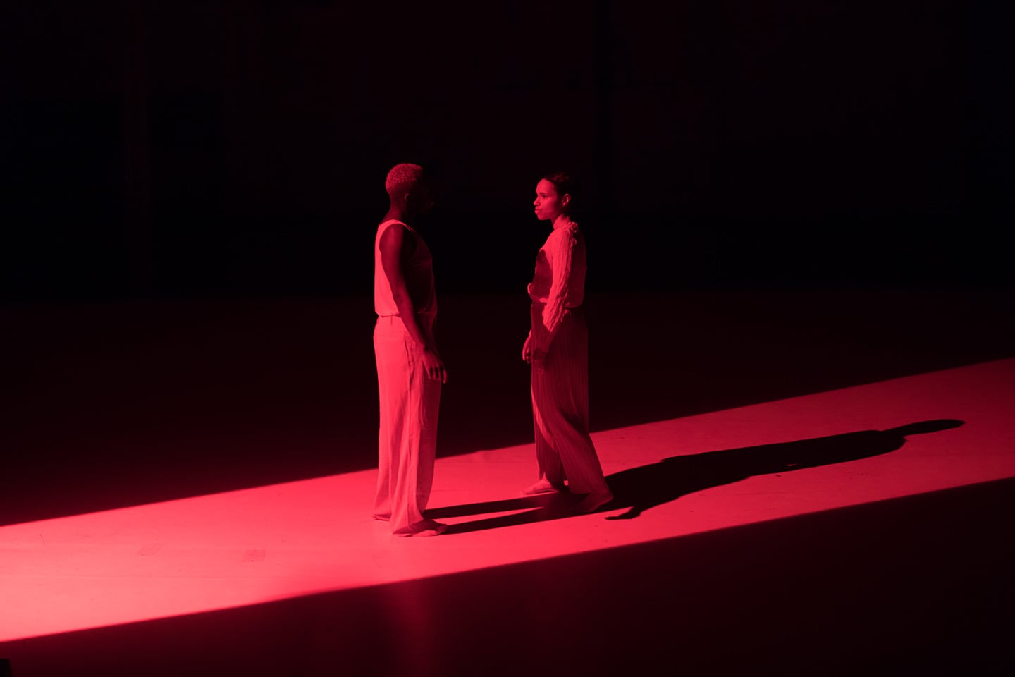 Two figures face each other in a strip of diagonal red light