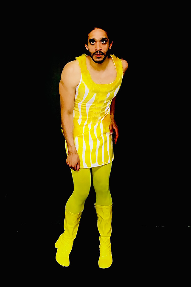 tall man with beard dressed as Twiggy in bright yellow short tunic-skirt, lime green tights and boots