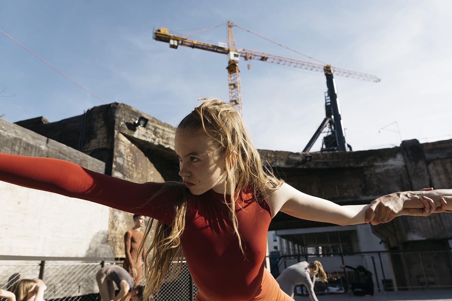 A crane in chimney as the background to a young female dancer in red leotard in the foreground, her arms stretching out to the edges of the frame