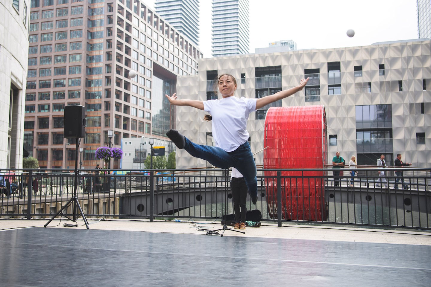 Against a backdrop of tall city buildings, a dancer leaps high in the air towards us