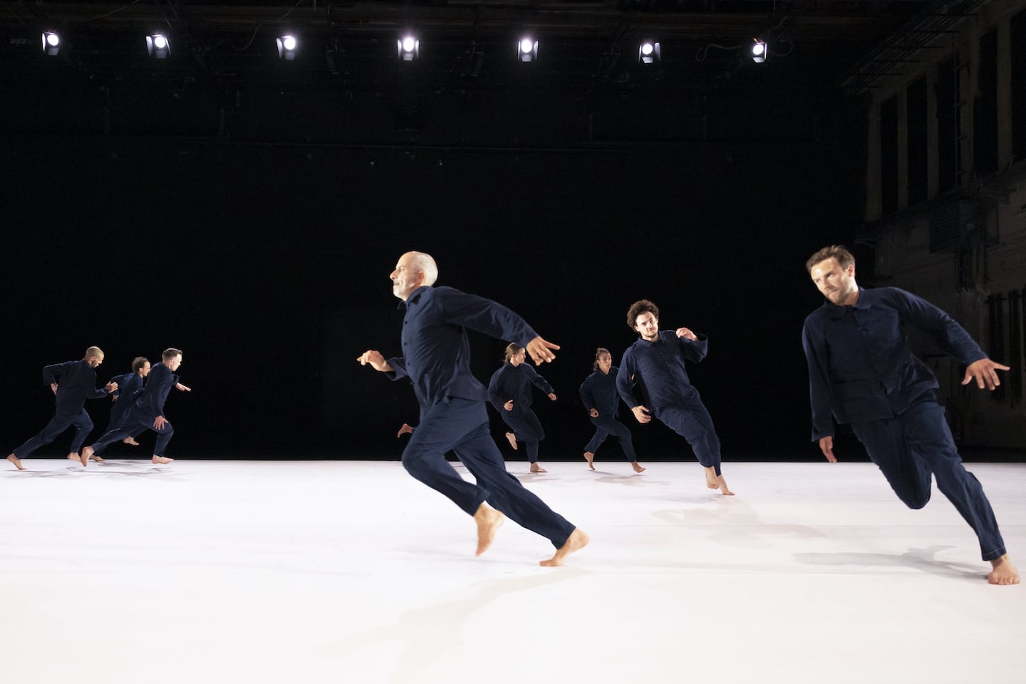 A group of people in navy blue overalls, running full tilt in a circle